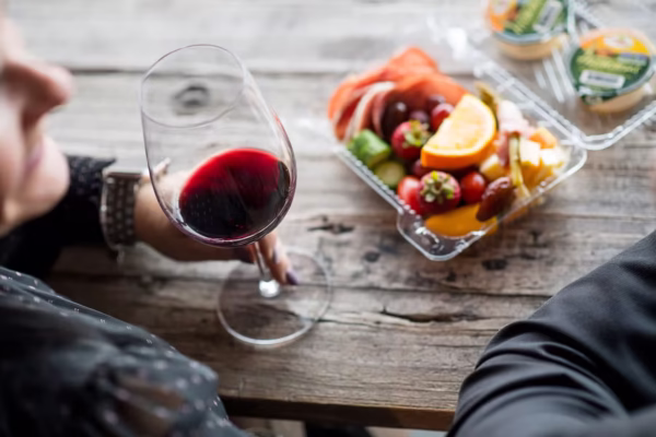 Woman holding a glass of red wine next to a platter of fresh fruits and snacks, reflecting a wine tour experience in the Okanagan region.