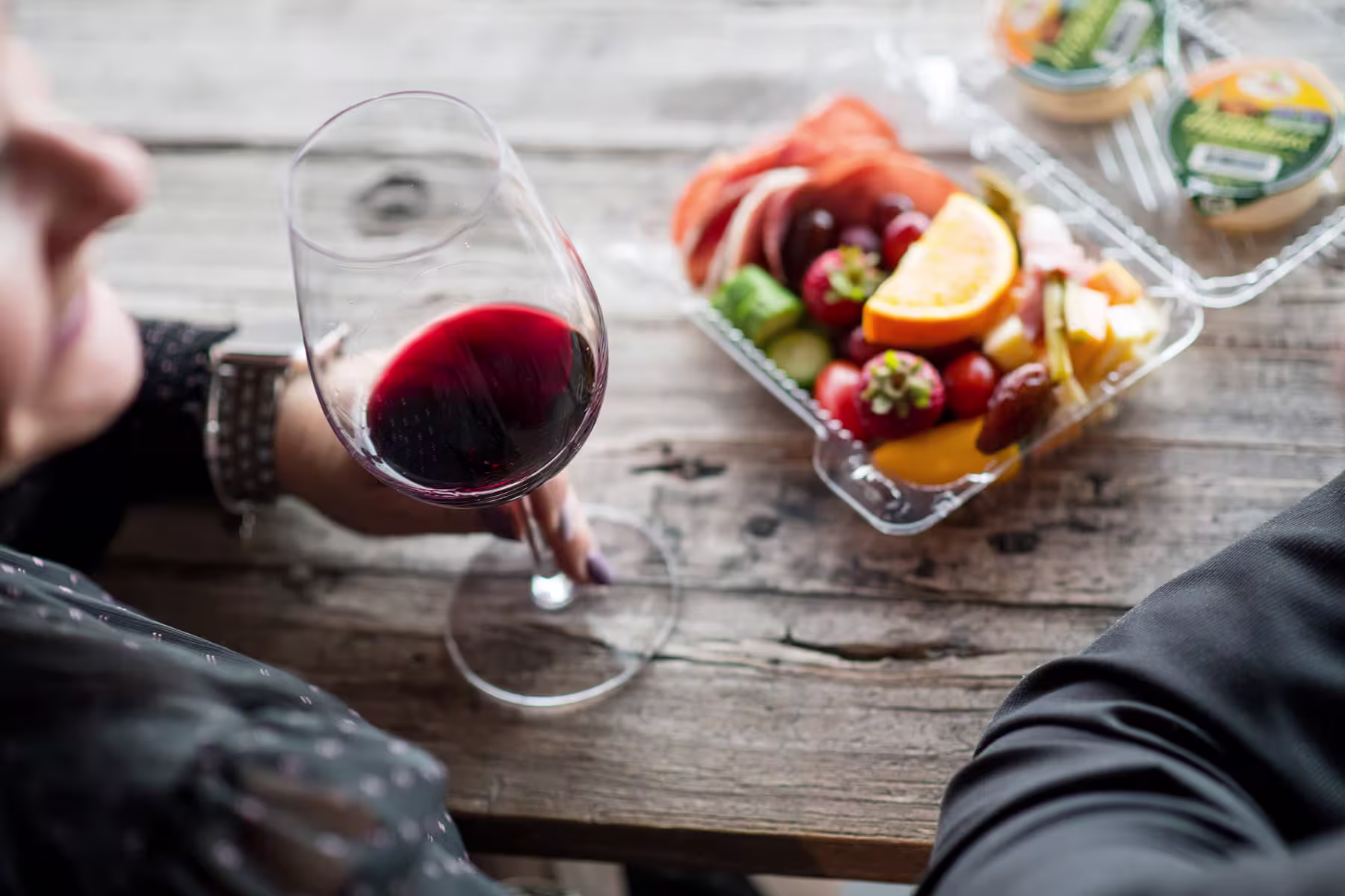Glass of red wine beside a platter of fresh fruits and vegetables on a rustic wooden table, highlighting the dining experience at Okanagan Resto.