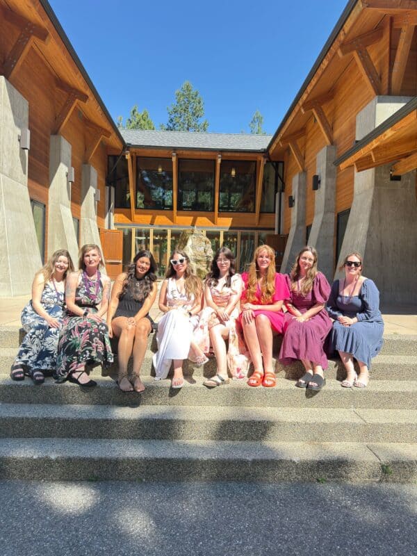 Group of women in summer dresses sitting on steps outside a modern building, showcasing a vibrant atmosphere ideal for Airbnb accommodations in the Okanagan region.